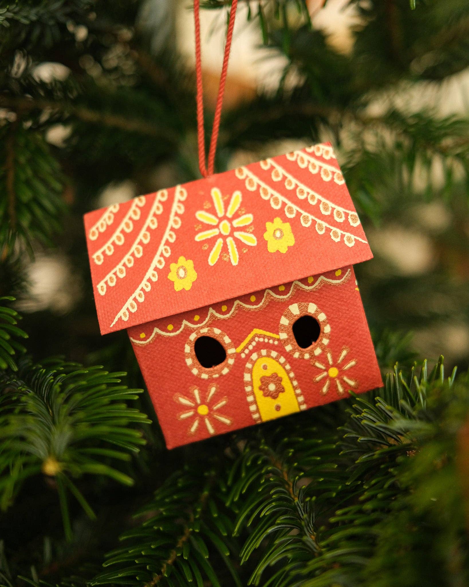Decorative red birdhouse ornament hanging on a Christmas tree.