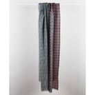 A long scarf with two vertical panels of intricate geometric and circular patterns, hanging from a white rod against a plain light gray wall.
