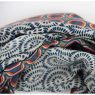 A close-up of a folded patterned fabric with a blue and red circular and spiral motif on a light background.