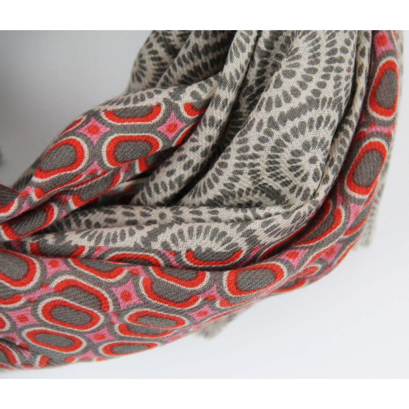 A close-up of a patterned scarf with a gray and beige base featuring circular medallion motifs in red, pink, and gray, set against a plain light gray background.