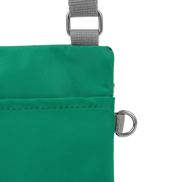 A close up photo of the back of an emerald green bag, showing the grey strap and neatly stitched pocket opening.