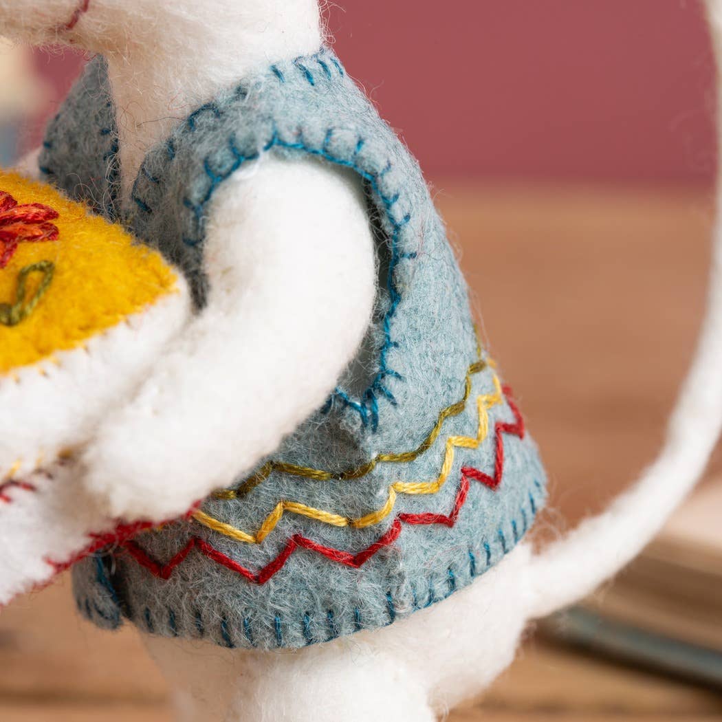 Close-up of a cat wearing a colorful sweater with embroidered patterns on a wooden floor.