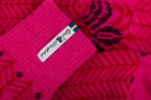 Close-up of a bright pink knit socks with a white fabric label and a small Swedish flag, showing the knit texture and patterned fabric.