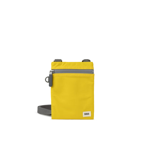 A photo of the front of a small rectangular yellow pocket bag. It has a grey zip horizontally at the top, grey straps, and a small ROKA logo in the bottom right corner.