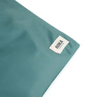 A close up photo of the bottom corner of a sage green bag, showing the ROKA London label.