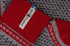 Close-up of a red knit sock with a white brand tag  and a small Swedish flag, laid over a gray and black patterned knit textile.