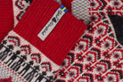 Close-up of a knitted socks showing a red ribbed cuff with a white tag alongside a red, gray, and black geometric pattern.