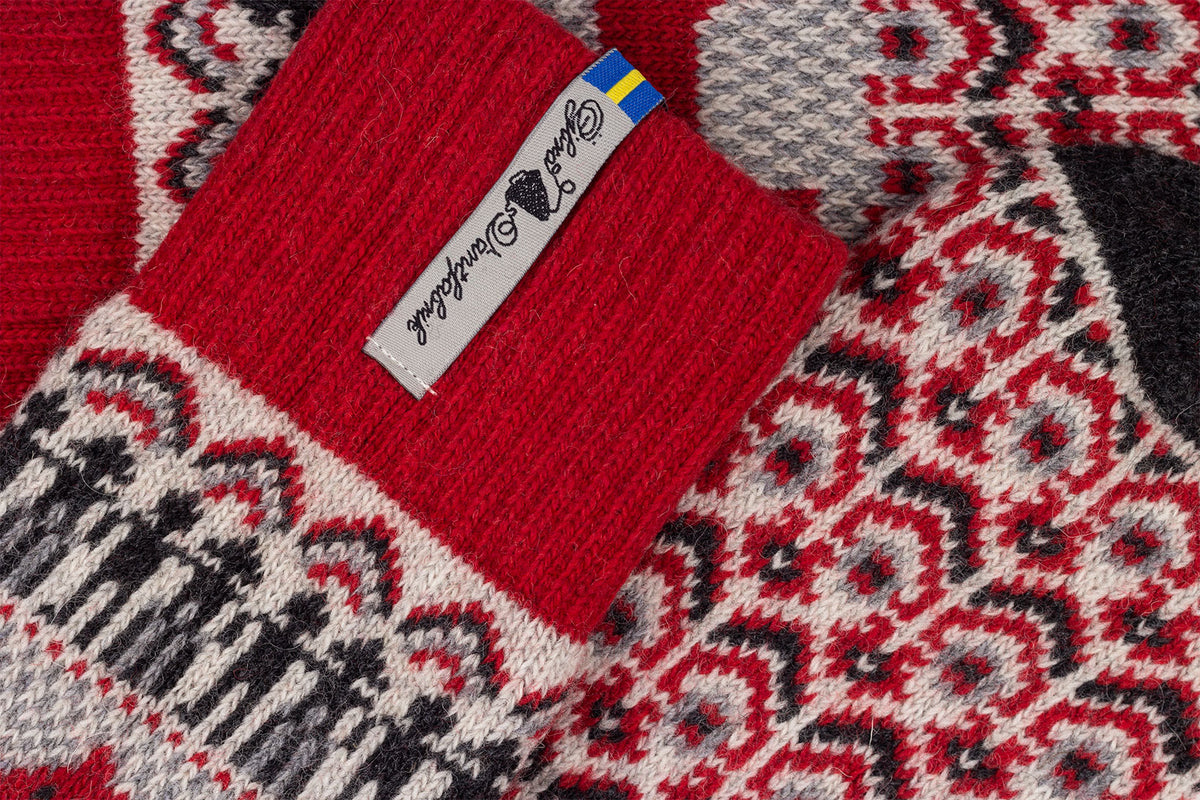 Close-up of a knitted socks showing a red ribbed cuff with a white tag alongside a red, gray, and black geometric pattern.